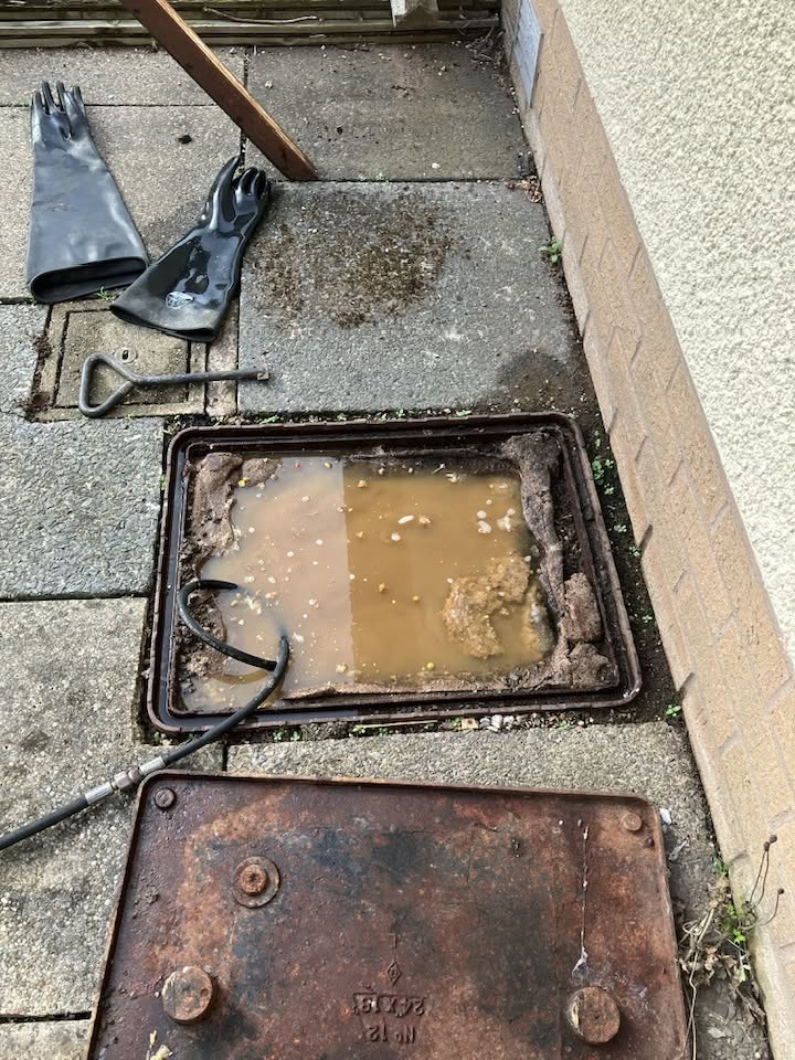 Blocked drain chamber full of murky water and debris